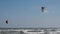 A man in a wetsuit on a parachute rides a board on the waves of the sea. A young man performs a trick in the air against