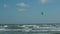 A man in a wetsuit on a parachute rides a board on the waves of the sea. A young man performs a trick in the air against