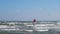 A man in a wetsuit on a parachute rides a board on the waves of the sea. A young man performs a trick in the air against