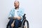 A man in a wheelchair smile, copy space, with tattoos on his arms sits on a gray studio background, the concept of