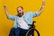 A man in a wheelchair smile and happiness, thumb up, with tattoos on his hands sits on a yellow studio background, the