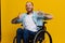 A man in a wheelchair smile and happiness, thumb up, with tattoos on his hands sits on a yellow studio background, the