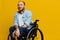 A man in a wheelchair smile and happiness, thumb up, with tattoos on his hands sits on a yellow studio background, the