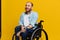 A man in a wheelchair smile and happiness, thumb up, with tattoos on his hands sits on a yellow studio background, the