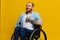 A man in a wheelchair smile and happiness, thumb up, with tattoos on his hands sits on a yellow studio background, the