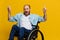 A man in a wheelchair smile and happiness, thumb up, with tattoos on his hands sits on a yellow studio background, the