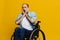A man in a wheelchair surprised, with tattoos on his arms sits on a yellow studio background, the concept of health is a