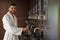 Man in white bathrobe drinking water, enjoying his day off at luxurious wellness spa center.