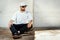 Man in a white cap is sitting on a skateboard in a concrete skatepark