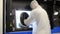 A man in a white protective suit stands near a large 3D printer