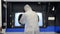 A man in a white protective suit stands near a large 3D printer