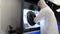 A man in a white protective suit stands near a large 3D printer