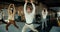 A man in a white shirt and glasses is doing yoga with his colleagues in the office