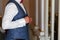 Man in a white shirt and a gray vest fastens buttons in front of the mirror. Groom in grey suit and tie getting ready in the morni