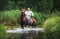 A man in a white shirt riding a horse crosses the river