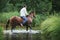 A man in a white shirt riding a horse crosses the river