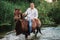 A man in a white shirt riding a horse crosses the river