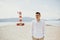 A man in a white shirt walks along the beach. The guy against the backdrop of mountains and the sea goes to the red lighthouse.