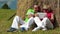 Man with white smartphone and woman with white tablet PC sits near a haystack