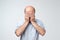 Man in white t-shirt covering his face with hands over white background.