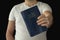 A man in a white T-shirt holds a bible in his hand.