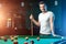 A man in a white T-shirt is playing billiards, a dark background. Pleasant pastime, entertainment, leisure, family holidays, games