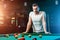 A man in a white T-shirt is playing billiards, a dark background. Pleasant pastime, entertainment, leisure, family holidays, games