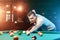 A man in a white T-shirt is playing billiards, a dark background. Pleasant pastime, entertainment, leisure, family holidays, games