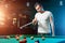 A man in a white T-shirt is playing billiards, a dark background. Pleasant pastime, entertainment, leisure, family holidays, games