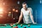 A man in a white T-shirt is playing billiards, a dark background. Pleasant pastime, entertainment, leisure, family holidays, games