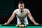 A man in a white T-shirt is playing billiards, a dark background. Pleasant pastime, entertainment, leisure, family holidays, games