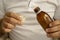 Man in a white t-shirt is pouring medical syrup in a measuring cup. A young man holds a bottle of syrup with a cup