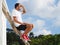 A man in a white T-shirt and red sneakers sits on a wooden staircase looking far.