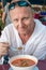 Man in a white tunic eats a spicy Thai soup Tom Yam in a cafe. Gastronomic tourism in Asia.