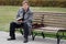 A man who looks like a writer or a fired clerk reads a book while sitting on a bench in an autumn park