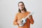 Man will rock you with his musician skill. Portrait of confident handsome guy in orange sweater holding ukulele, pulling