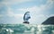 A man wing foils at sea using a hand held inflatable wing, riding a hydrofoil surfboard.  Turquoise sea, cloudy blue sky.