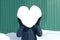 Man in winter clothes with big heart made of snow instead his head, on the green wall background. Declarations of love, valentines