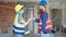 Man and woman builders shake hands holding blueprints at construction site