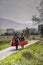 Man and woman carry two canoes along single track road, Glencoe, Scotland.