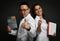 Man and woman couple doctors show thumbs up with books on dark background