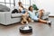 Man and woman couple sitting on sofa with dogs cleaning floor using vacuum robot at home