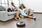 Man and woman couple sitting on sofa with dogs cleaning floor using vacuum robot at home