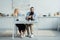 Man and woman drinking coffee and playing with french bulldog on kitchen table