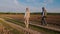 A man and a woman, a farmer couple, stroll along a country road adjacent to a plowed field.. Back view