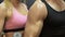 Man and woman flexing arms simultaneously by lifting dumbbells, workout in gym