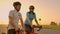 A man and a woman in helmets with bicycles stand and talk at sunset. Rest after a bike ride on the highway. Track bikes