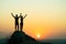 Man and woman hikers standing on a big stone at sunset in mountains. Couple raising up hands on high rock in evening nature.