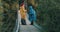 Man and woman hikers, walking on bridge over river, drinking from vacuum flask