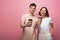 Man and woman hoding paper cups and smiling at camera on pink background